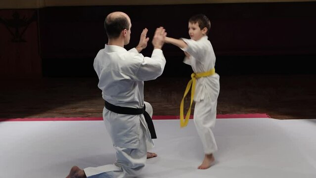 A coach trains a small child athlete to throw punches on the palms of his hands
