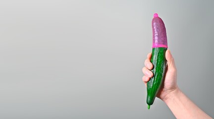 Unrecognizable person holding a cucumber with Red condom. Panoramic image with copy space. Safe sex...