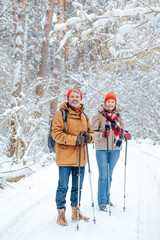Man and woman with scandinavian sticks in a winter forest looking enjoyed