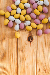 Multi-colored chocolate decorative eggs on a wooden background with sun reflections. Happy Easter background. Top view