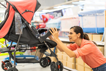 Mother woman carefully examines a modern, decision making stroller in spacious baby store, mindful...