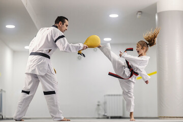 A taekwondo kid is kicking kick pad and training with her coach at martial art school class.