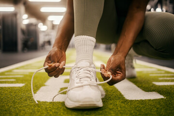 Close up of a black sportswoman's hands tying shoelace on shoelace on sneaker at gym.