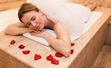 Hammam marble table warms body of beautiful woman before foam massage procedure in Turkish bath. Hammam in spa
