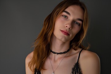 Person with shoulder-length hair and subtle makeup gives a soft gaze wearing a choker and a necklace