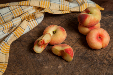 Half and several whole saturn peaches or flat peaches on wooden background with yellow kitchen...