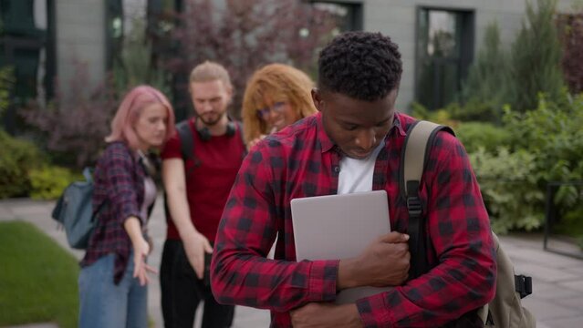 Stressed African American school guy male student bullied man suffer with racism discrimination bullying multiracial students classmates mock humiliate bully mockery at college university outdoors