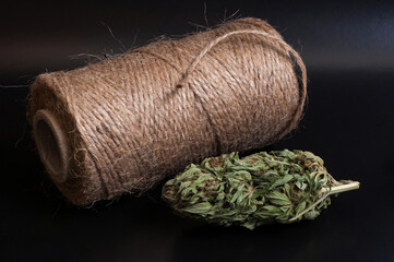 still life of spool of hemp rope with dried marijuana bud and small glass filled with cannabis...