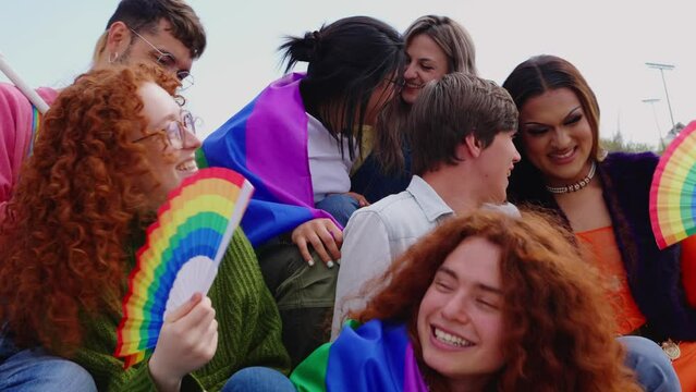 LGBT community young people celebrating gay pride month together outdoors. Diversity LGBTQ group with rainbow flag having fun at city street. 