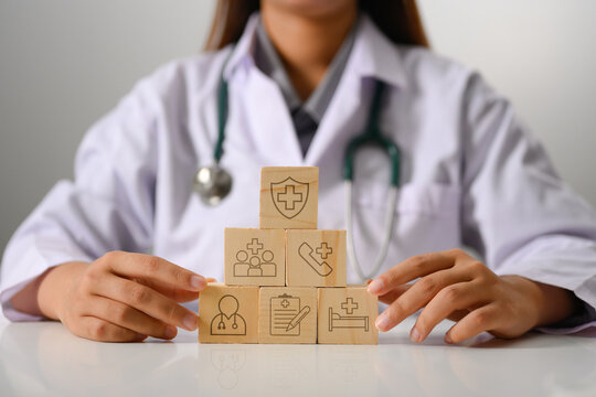 Doctor touching wooden cubes stack in pyramid shaped with medical insurance icons