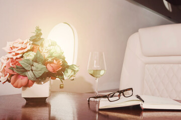 Luxury decor of salon private jet with flowers, diary, wine glass, glasses on table. Comfort vip...