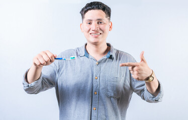 Man holding and recommending a toothbrush. Smiling guy holding and pointing at toothbrush isolated....
