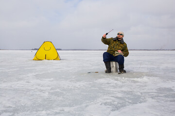 A man fishes on the ice of a lake. A fishing tent stands on the ice of a lake.
