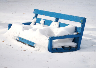 Winter background .Blue wooden bench covered with snow in the park.