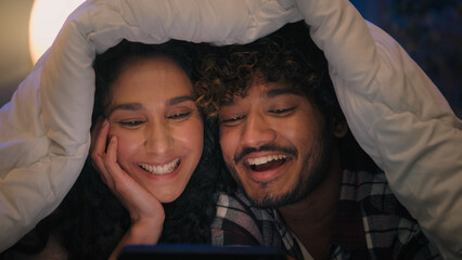 Multiracial happy carefree couple Indian man Hispanic woman watching film movie funny video...
