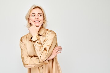 Woman in beige blouse smiling, looking away with thoughtful expression isolated on light background.