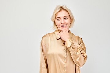 Smiling woman posing with hand on chin against a light background, expressing thoughtfulness.