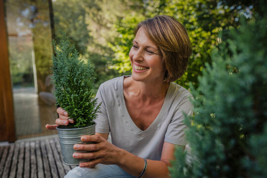 gl&uuml;ckliche Frau mit Blumentopf vor einer neuen Immobilie, Bayern, Deutschland