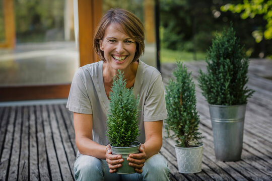 gl&uuml;ckliche Frau mit Blumentopf vor einer neuen Immobilie, Bayern, Deutschland