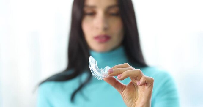 Young woman holds plastic transparent mouth guard in hands. Bite alignment concept