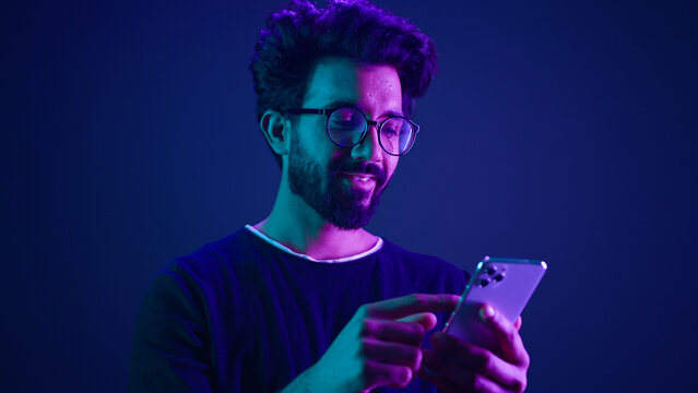 Arabian male using mobile phone chatting browsing smartphone online order shopping gaming with cellphone Indian man scrolling social media internet technology app at neon ultraviolet studio background