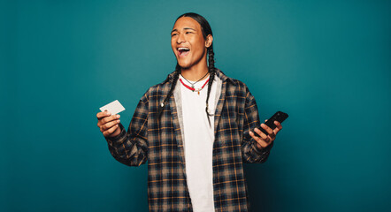 Happy native man smiling with braided hair pays online using credit card on blue studio background - 756361109