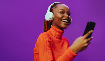 Young woman listening to music on purple background