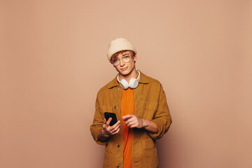 Happy young man using smartphone on vibrant peach background - 756361190