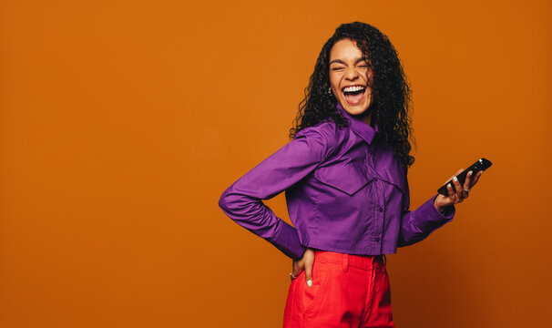 Vibrant orange background: Cheerful woman using smartphone for social media messaging