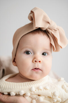A beautiful little girl with big eyes and a big bow headband on her head. Cute Baby, 6 months old closeup. Portrait of an adorable baby girl with bow in hair isolated in white background.
