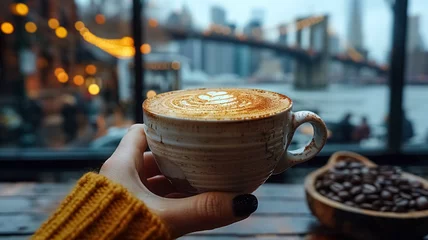 Foto op Plexiglas Close-up of a female hand holding a cup of coffee and Brooklyn Bridge is in the background, first-person photo, blurred background, travel image with well known destination © Loucine