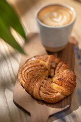 Cup of cappuccino with cinnamon roll on the cutting board. Selective focus.