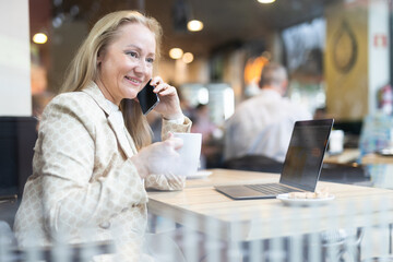 Businesswoman sitting at cafe table and talking on mobile phone