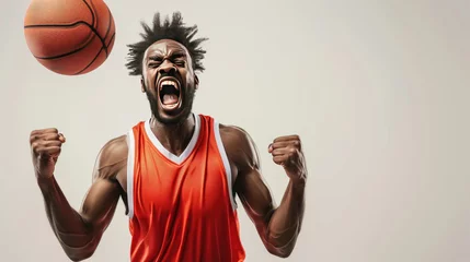 Fotobehang A basketball player in an orange jersey is holding a basketball and yelling © kiatipol