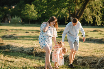 Naklejka na ściany i meble Mother, father hold hands happy children daughter. Running in green grass in nature on summer day. Concept of family spending time together on a picnic. Mom, dad, and kids walking in park at sunset.