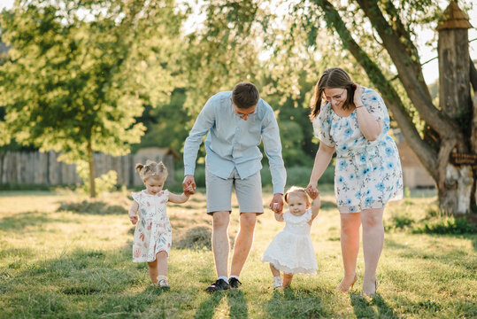Mother, father hold hands happy children daughter. Running in green grass in nature on summer day. Concept of family spending time together on a picnic. Mom, dad, and kids walking in park at sunset.