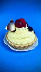 a tartlet with custard decorated with a piece of chocolate, grapes and strawberries is depicted on a blue background. dessert. side view. Birthday