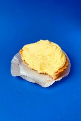 A bitten-off pie tartlet with yellow custard lies on a blue background. side view . a half-eaten dessert