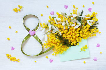 Greeting card for International Women's Day March 8. White wooden background with envelope, mimosa flowers, snowdrops, hearts and number eight from ribbon. - 756376799