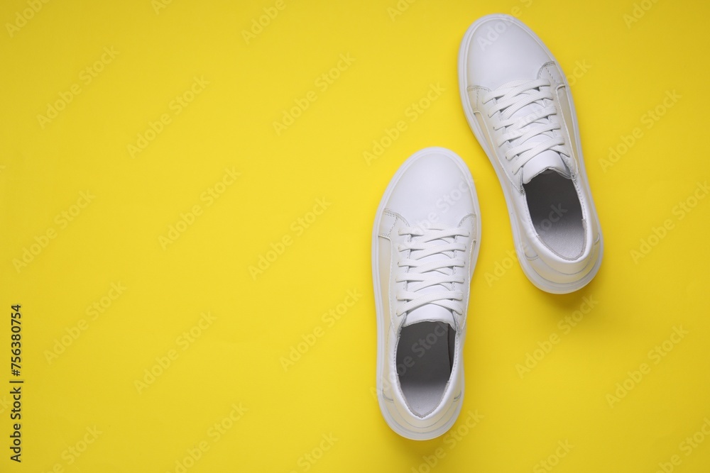 Wall mural Pair of stylish white sneakers on yellow background, top view. Space for text