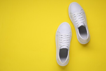 Pair of stylish white sneakers on yellow background, top view. Space for text