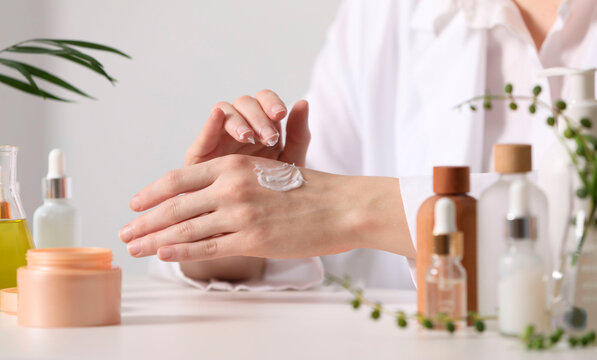 Dermatologist applying cream onto hand at white table indoors, selective focus. Testing cosmetic product