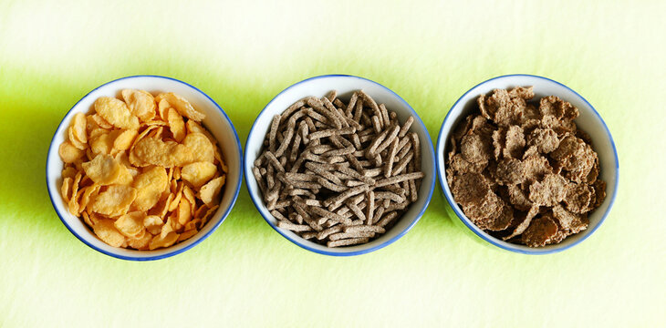 Diversi tipi di cereali da colazione secchi in ciotole isolate su sfondo verde pastello. Vista dall'alto. Copia spazio.
