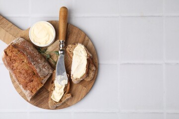 Tasty bread with butter and knife on white tiled table, top view. Space for text