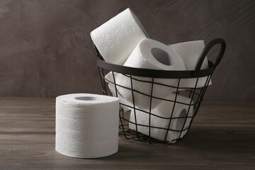 Soft toilet paper rolls in metal basket on wooden table, closeup
