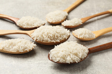 Fototapeta na wymiar Raw basmati rice in spoons on grey table, closeup