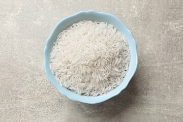 Raw basmati rice in bowl on grey table, top view