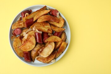 Delicious baked potato with thin dry smoked sausages and onion on yellow table, top view. Space for text