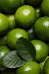 Fresh ripe limes and leaves as background, top view