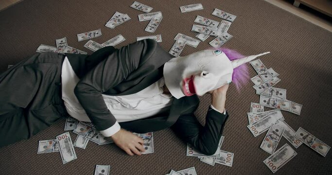 Businessman with unicorn mask counting stack cash money dollar profit salary wage earnings on workplace. Concept of salary or profit. Handsome happy businessman with unicorn mask scatters the dollars.